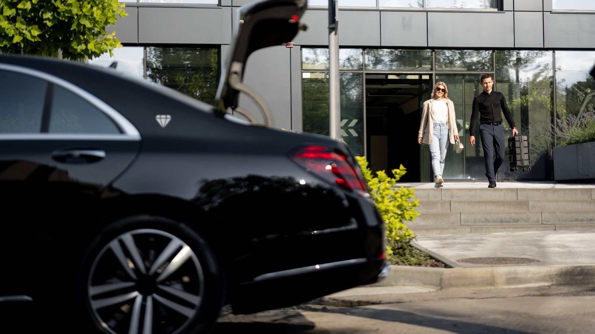 Shuttle D'Luxe chauffeur carrying a passenger's luggage to a black sedan